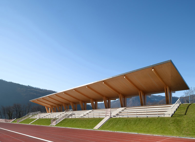 Nadstrešek Brajda v Tolminu z lesenim stropom nad tribunami in pogledom na okoliške hribe.